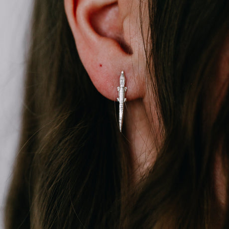 A close-up image of a person's ear wearing a silver-colored alligator earring.