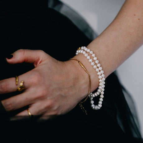 A person wearing a gold-plated bracelet with white beads and a single pearl, made in Sweden